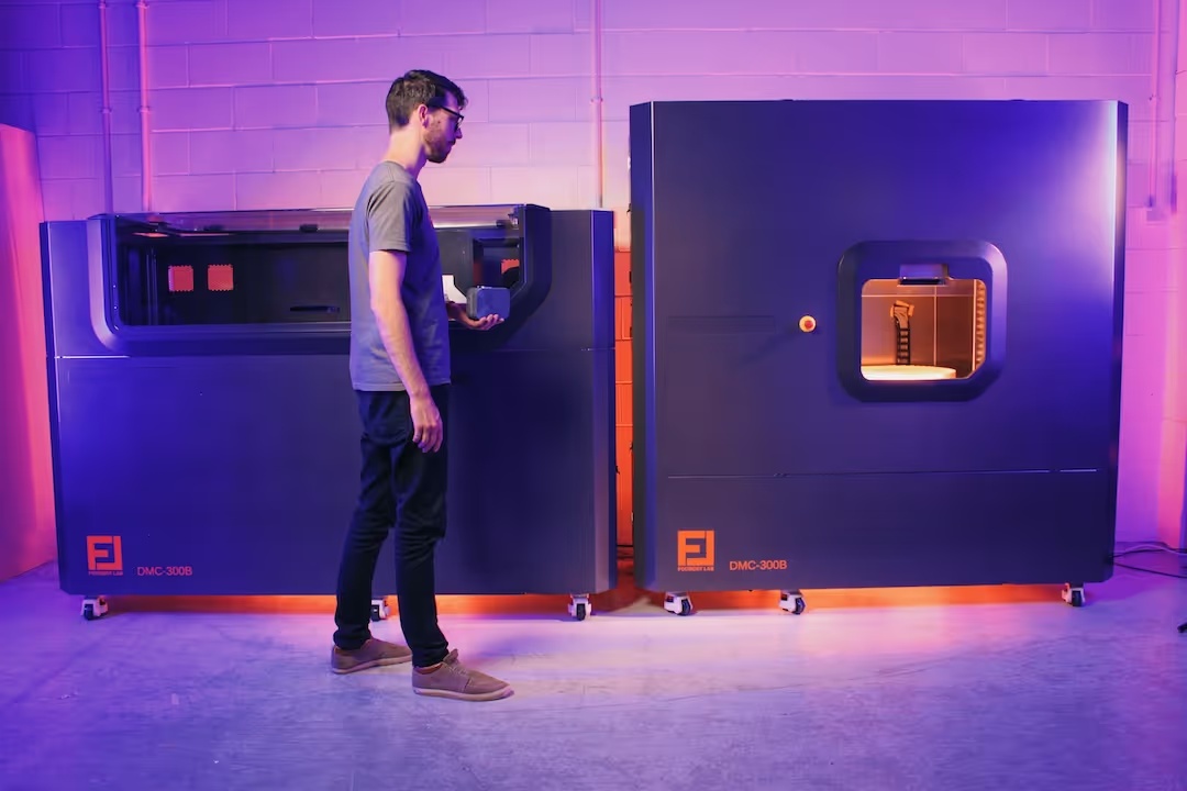 David Moodie holding a component beside two Foundry Lab casting machines