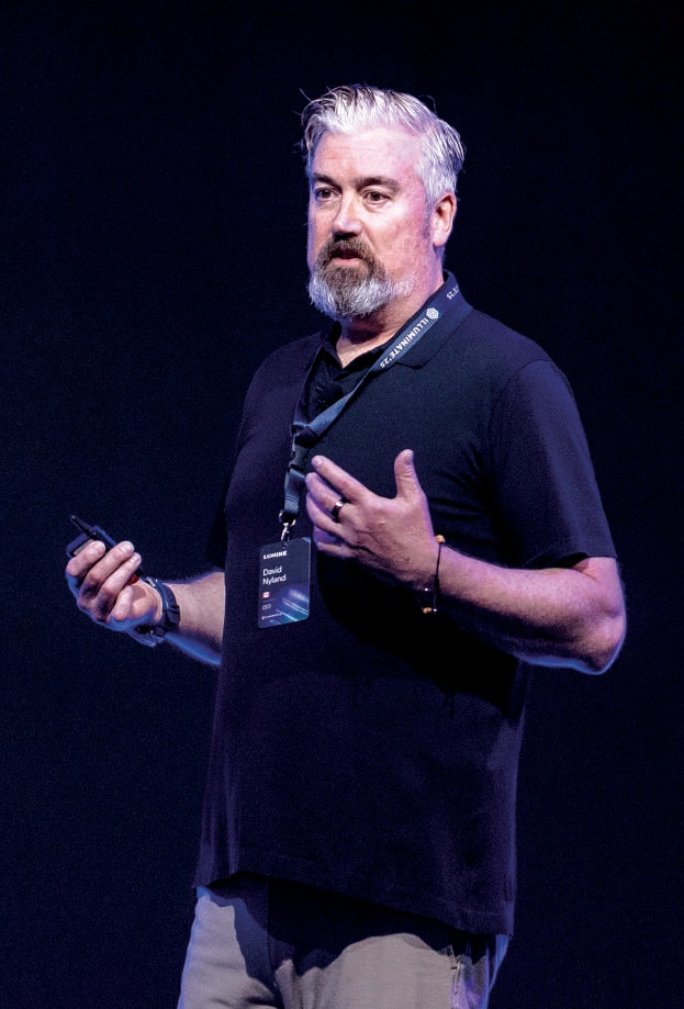 David Nyland speaking on stage, holding a presentation clicker