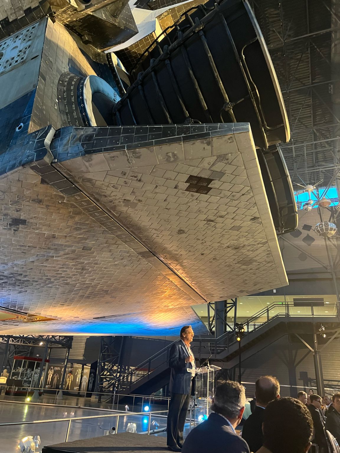 David Rowe speaking at a lectern beneath a space shuttle during AE Industrial Partners’ 2023 annual meeting