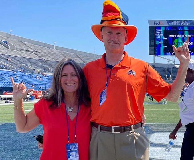 Jennifer and David Spencer cheering for UTSA in Memphis in 2021, with David wearing an orange Roadrunner hat