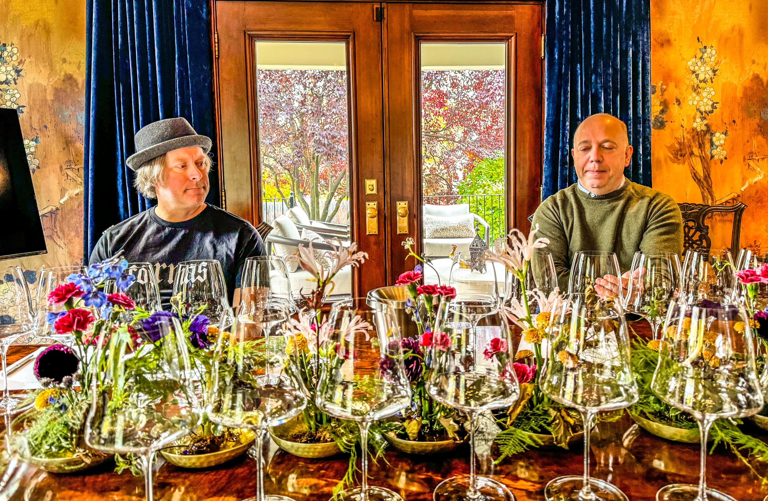 Winemaker Todd Alexander, left, and David Wanek, right, seated at a tasting table filled with wine glasses and flowers.