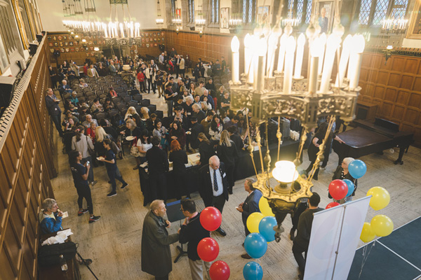 A crowd gathers beneath chandeliers in the wood-panelled Great Hall during the Open Hart House centennial event