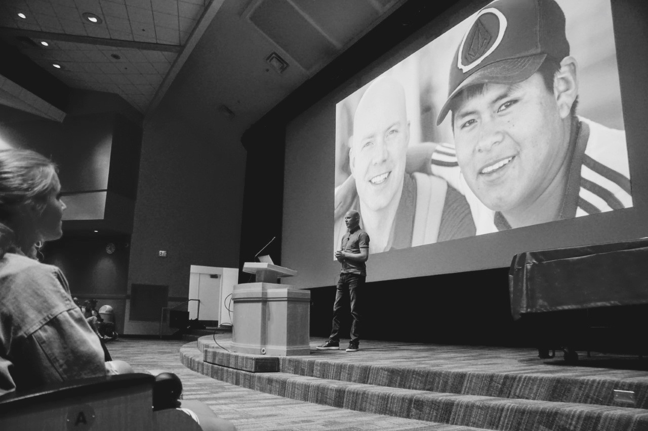 Davis Smith speaks onstage at BYU with a photograph of himself and Edgar projected behind him