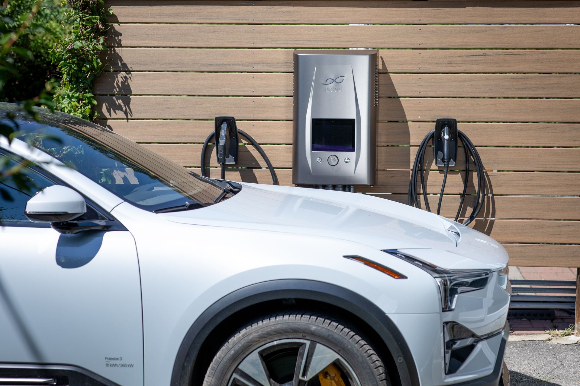 A white Polestar 3 parked beside a dcbel home energy station and two charging connectors