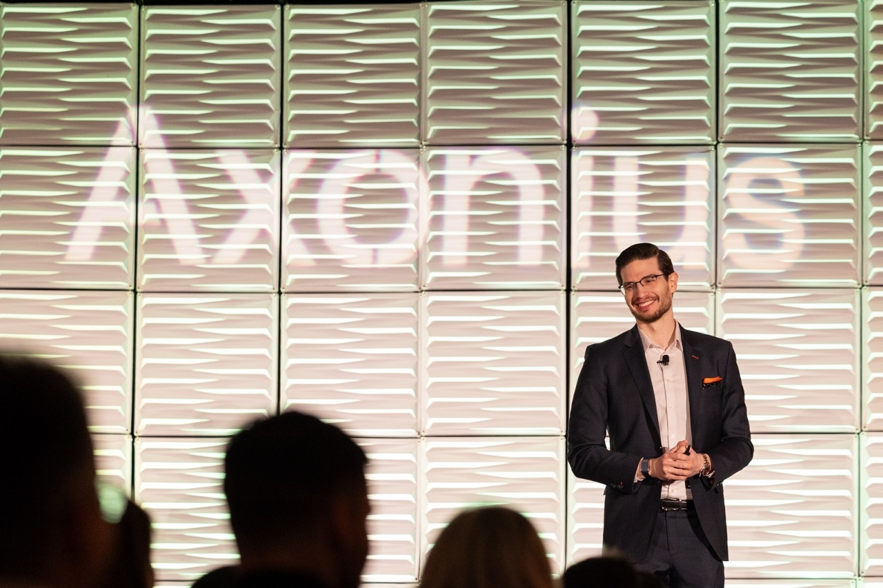 Dean Sysman speaking on a stage with Axonius projected behind him