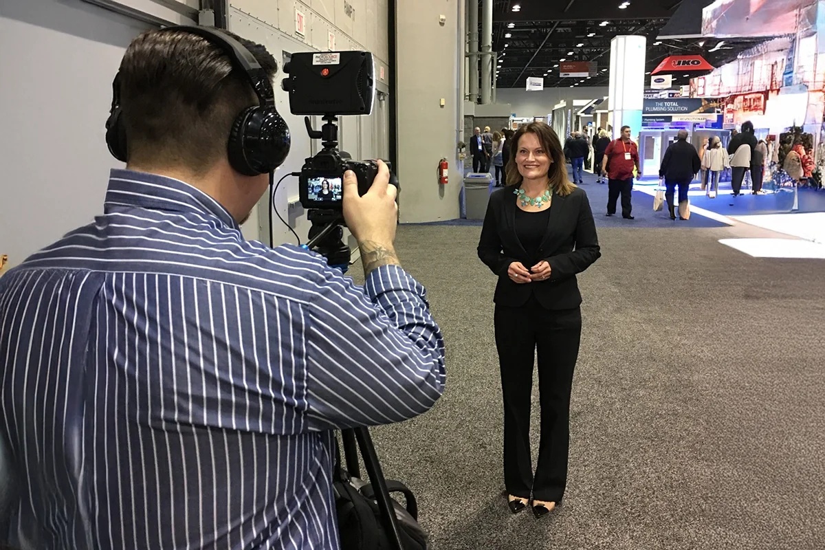 Debi Hammond being filmed by a camera operator in a busy trade-show hallway