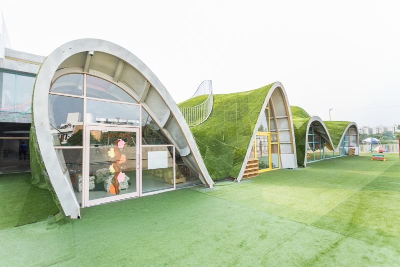 Curved school buildings and a green play area at Toddler’s Den in 2017