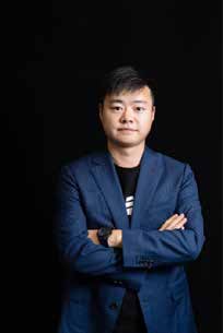 Del Wang in a blue blazer with folded arms against a black background, in a 2021 conference brochure