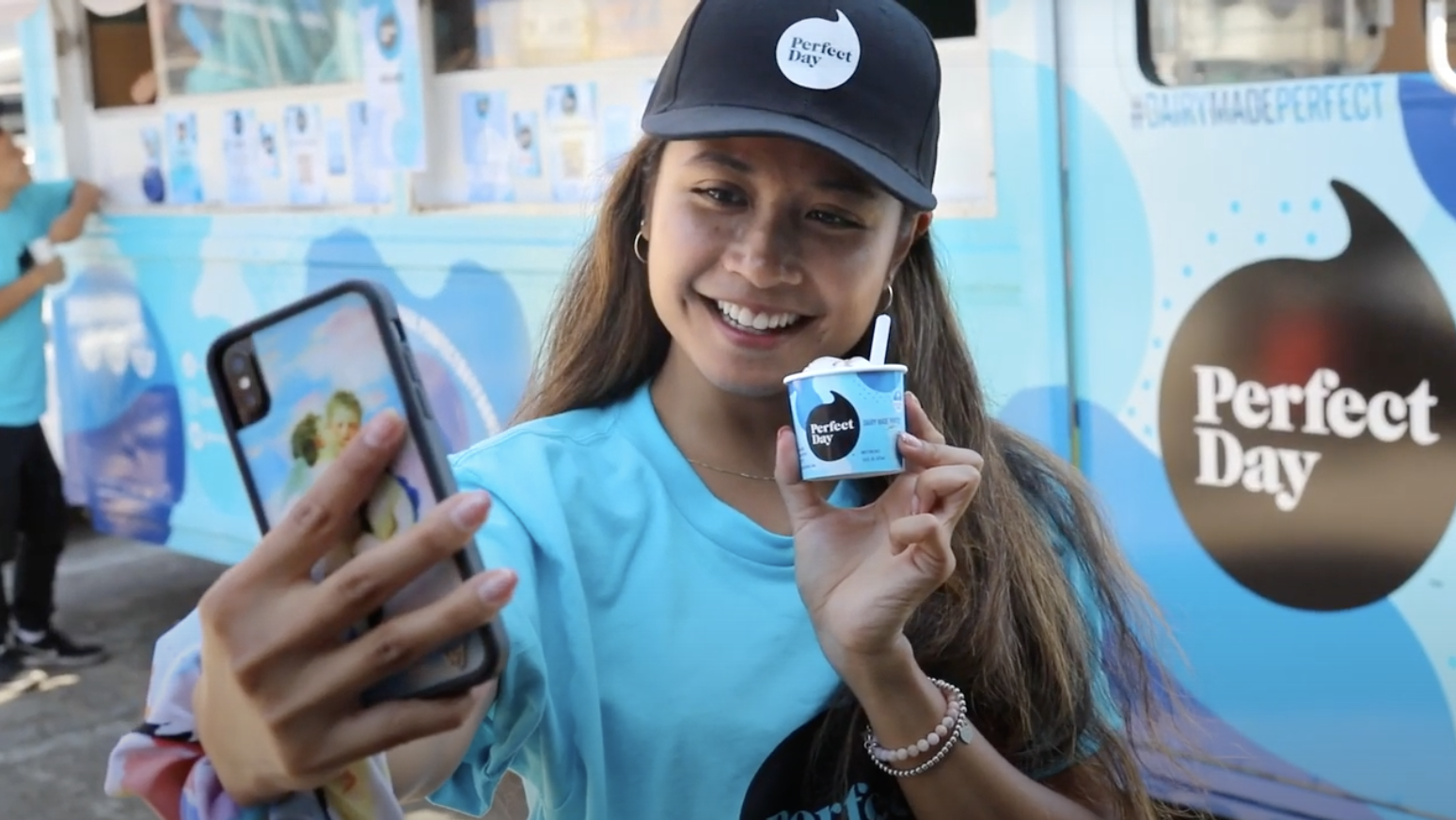 A participant holds a Perfect Day ice-cream cup and takes a selfie beside a branded truck
