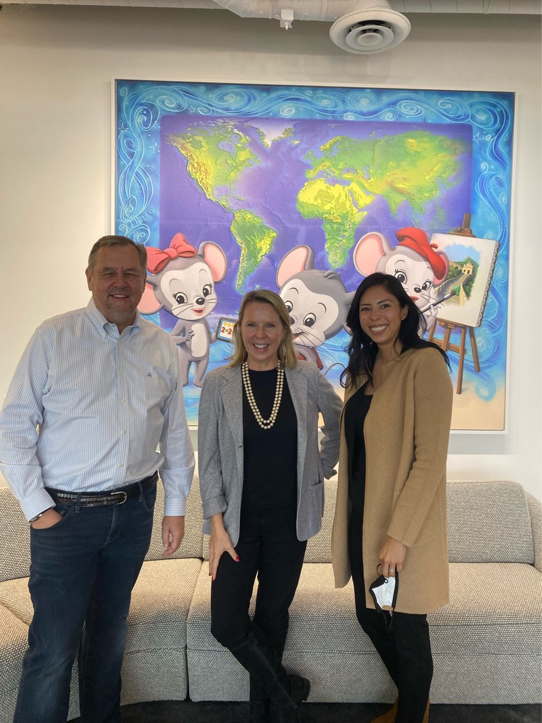 Doug Dohring, Dena Cook and Jennifer Reza standing together at Age of Learning, with an illustrated world map behind them.