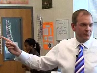 Archival photograph of Denis Brosnan gesturing while speaking in a classroom
