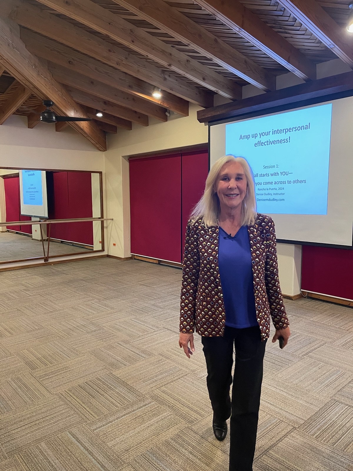 Denise Dudley standing in a workshop room beside a presentation on interpersonal effectiveness