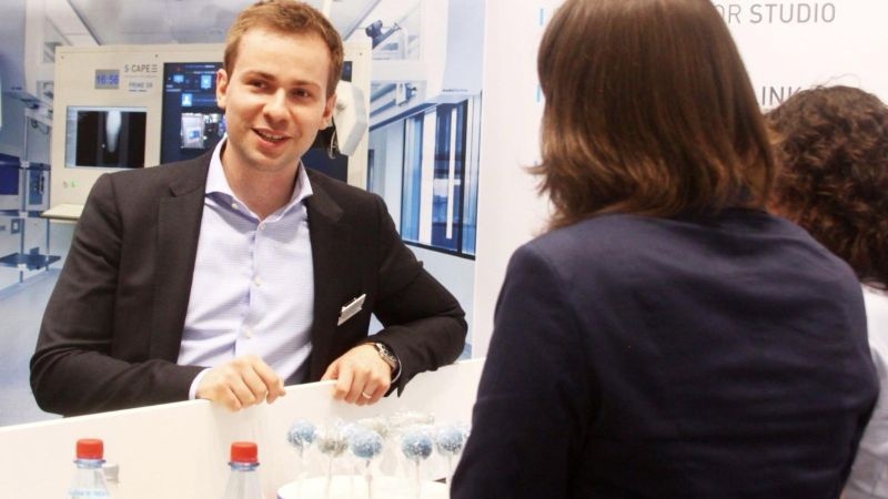A younger Dennis Kogan, at left, speaking with visitors across a table at an exhibition stand