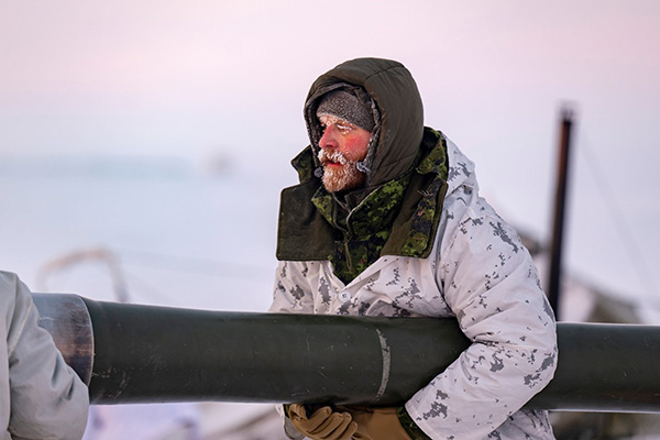 A frost-covered Canadian soldier in winter camouflage handles an M777 howitzer barrel during Operation NANOOK-NUNALIVUT in Nunavut.