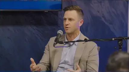 Derik Sutton speaking into a microphone during a live Banking on Community discussion at CX26