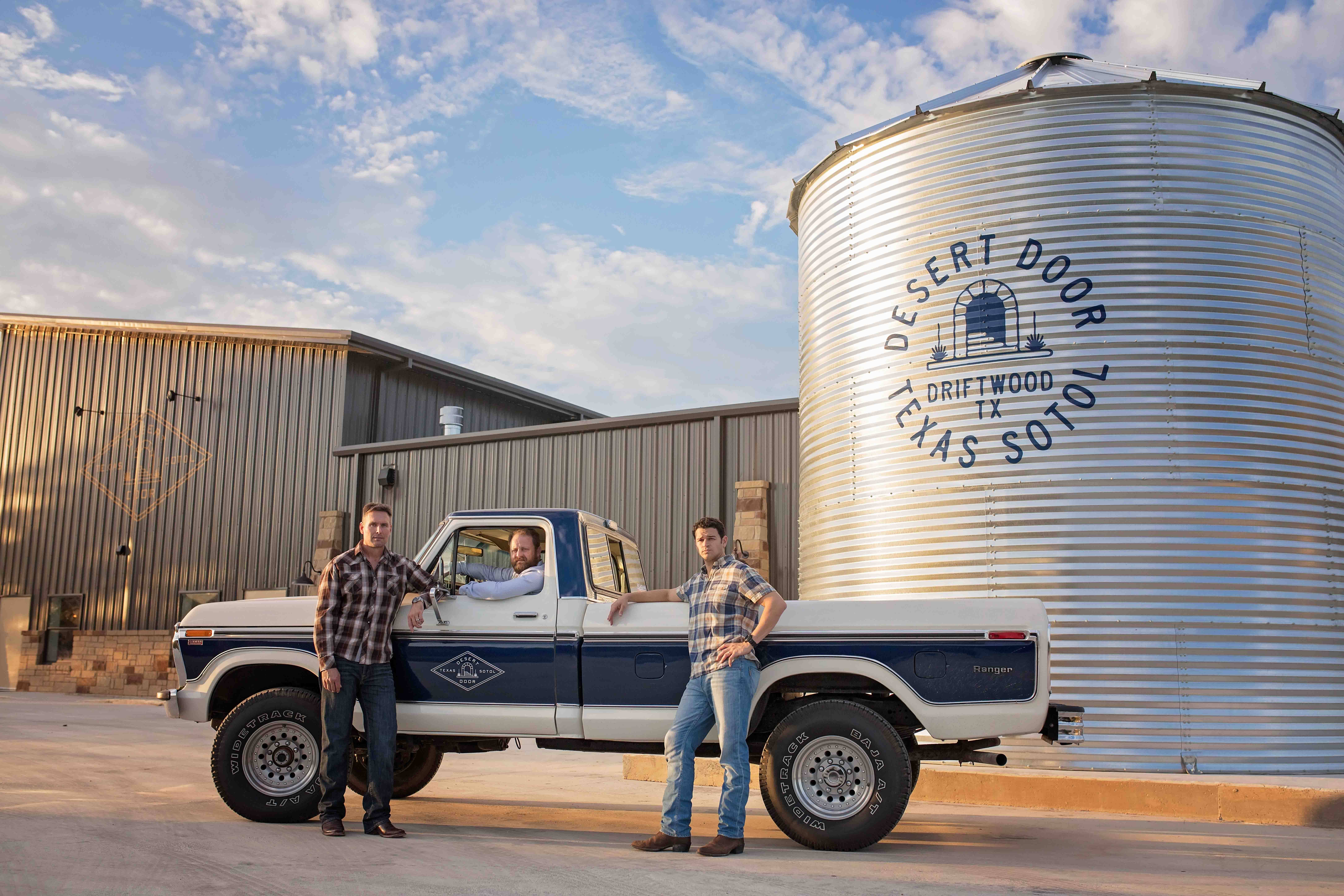 Desert Door’s three founders beside a pickup truck outside the Driftwood distillery