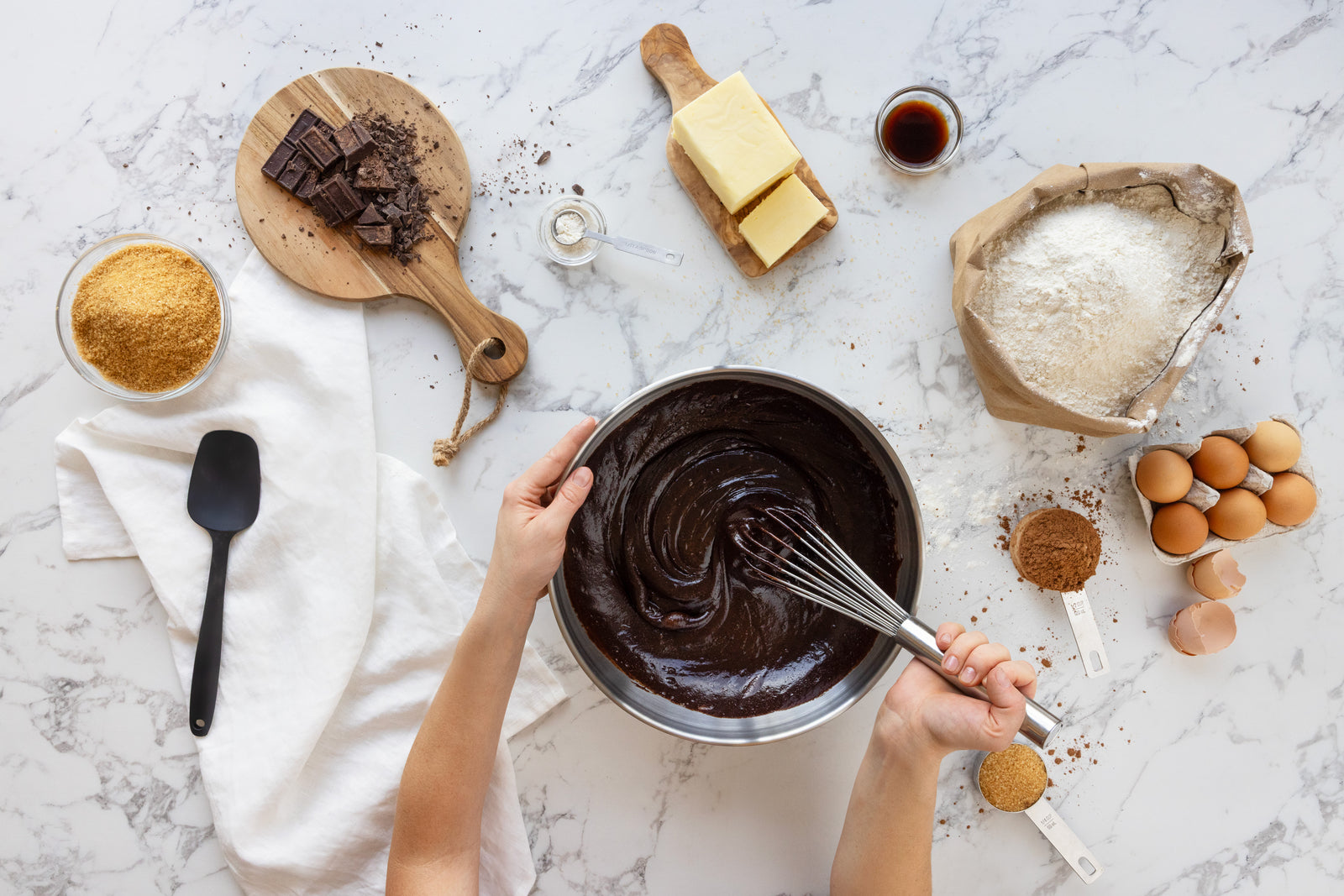 Hands whisking chocolate batter surrounded by baking ingredients