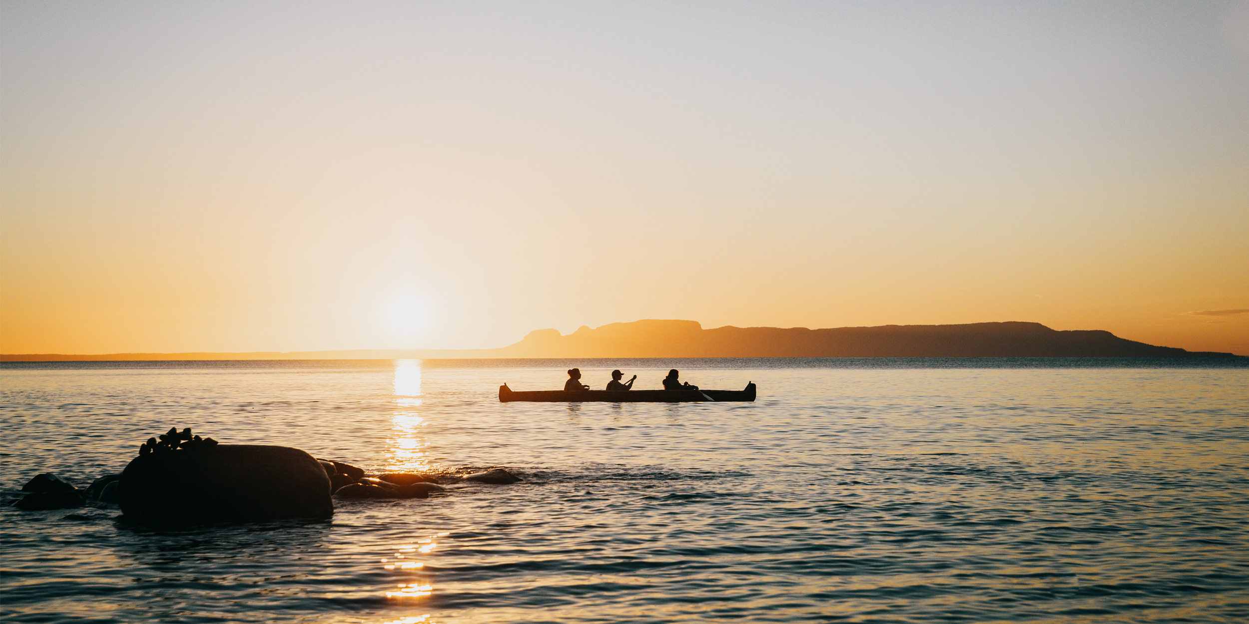 Canoeists cross calm water at sunset near Pass Lake, Ontario