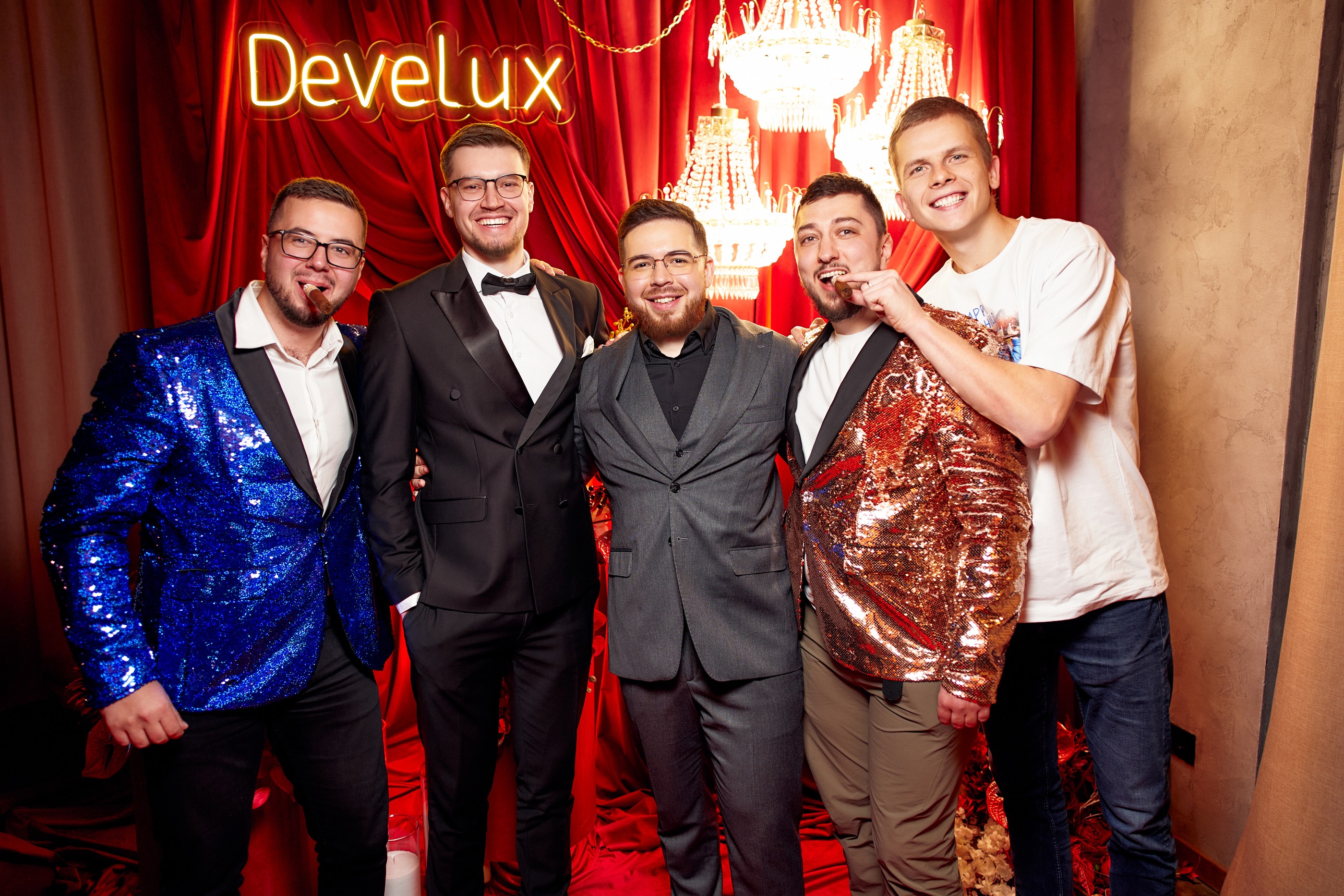 A group poses in front of red curtains and an illuminated Develux sign at a company event