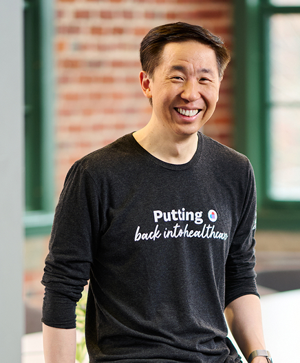 Devoted Health co-founder and CEO Ed Park smiling in front of a brick wall