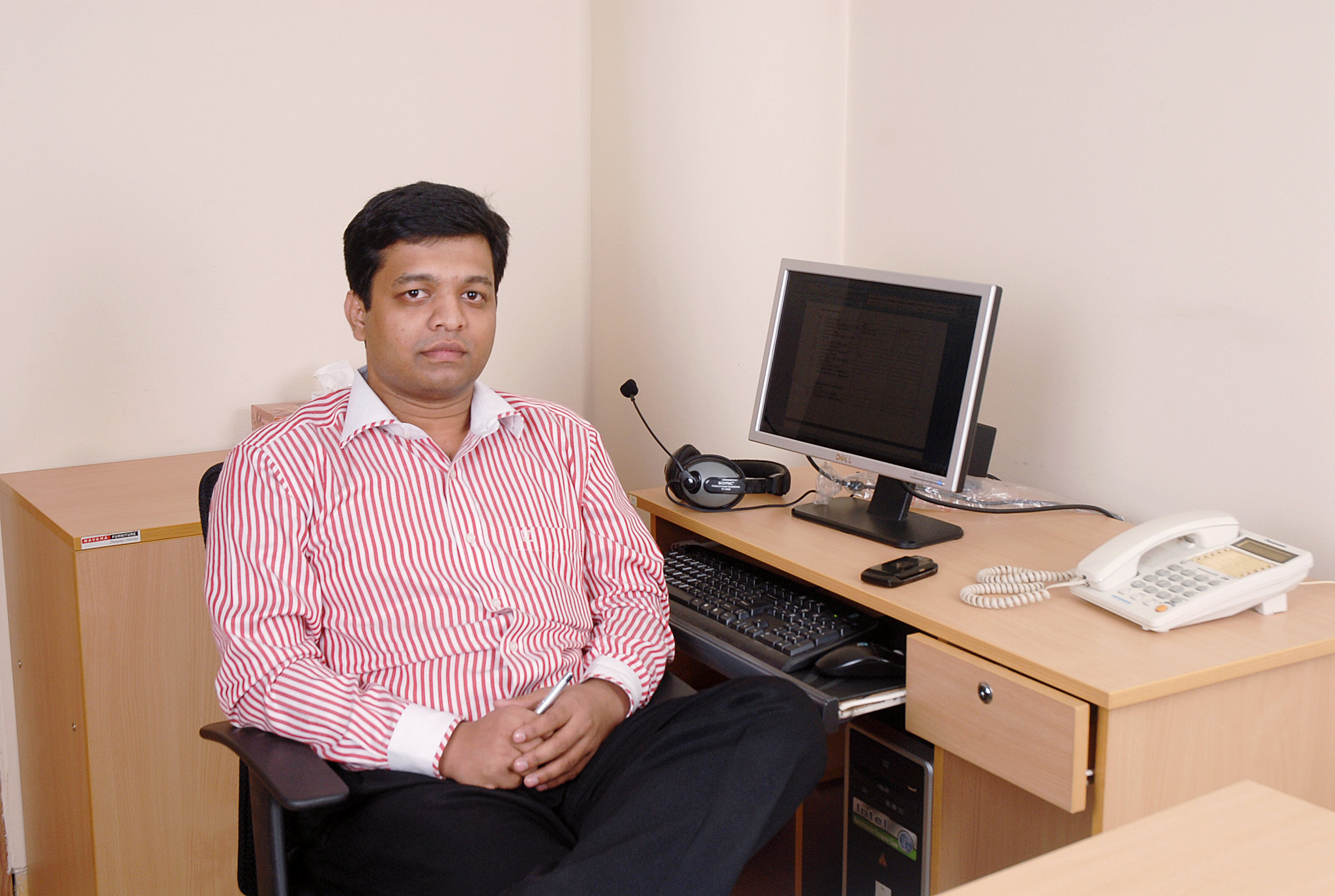 Dewan Shuvo seated at an office desk beside a monitor, headset and telephone