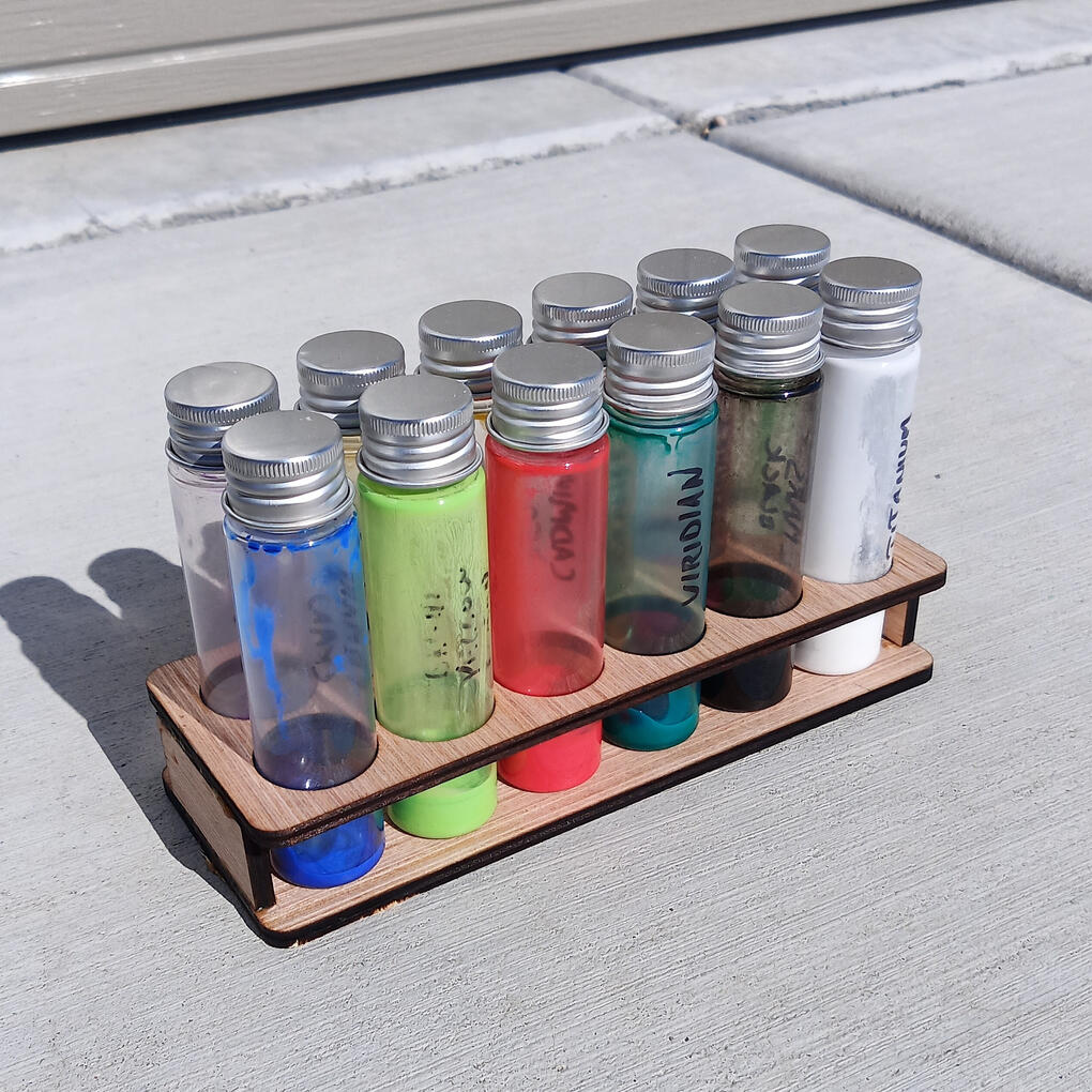 Paint-filled glass tubes standing in a two-tier laser-cut wooden holder