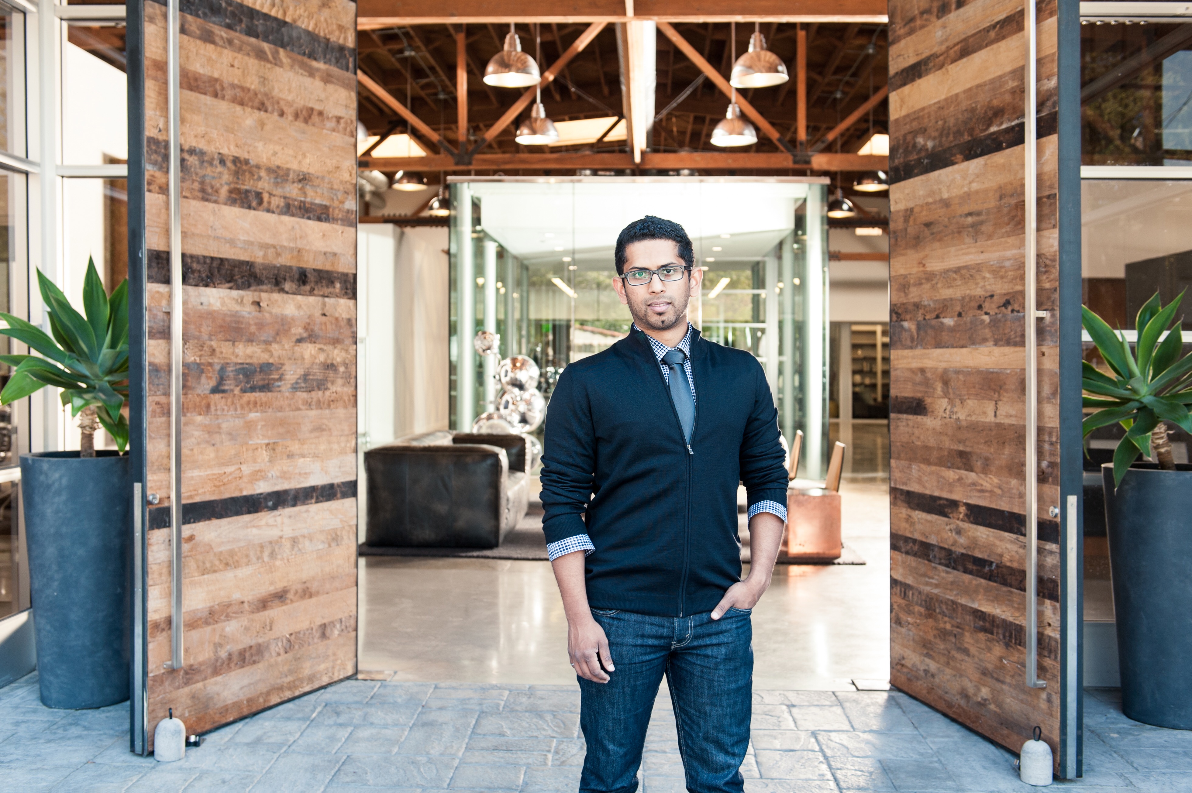 DJ Jayalath standing between open wooden doors in a photograph published with his 2016 interview