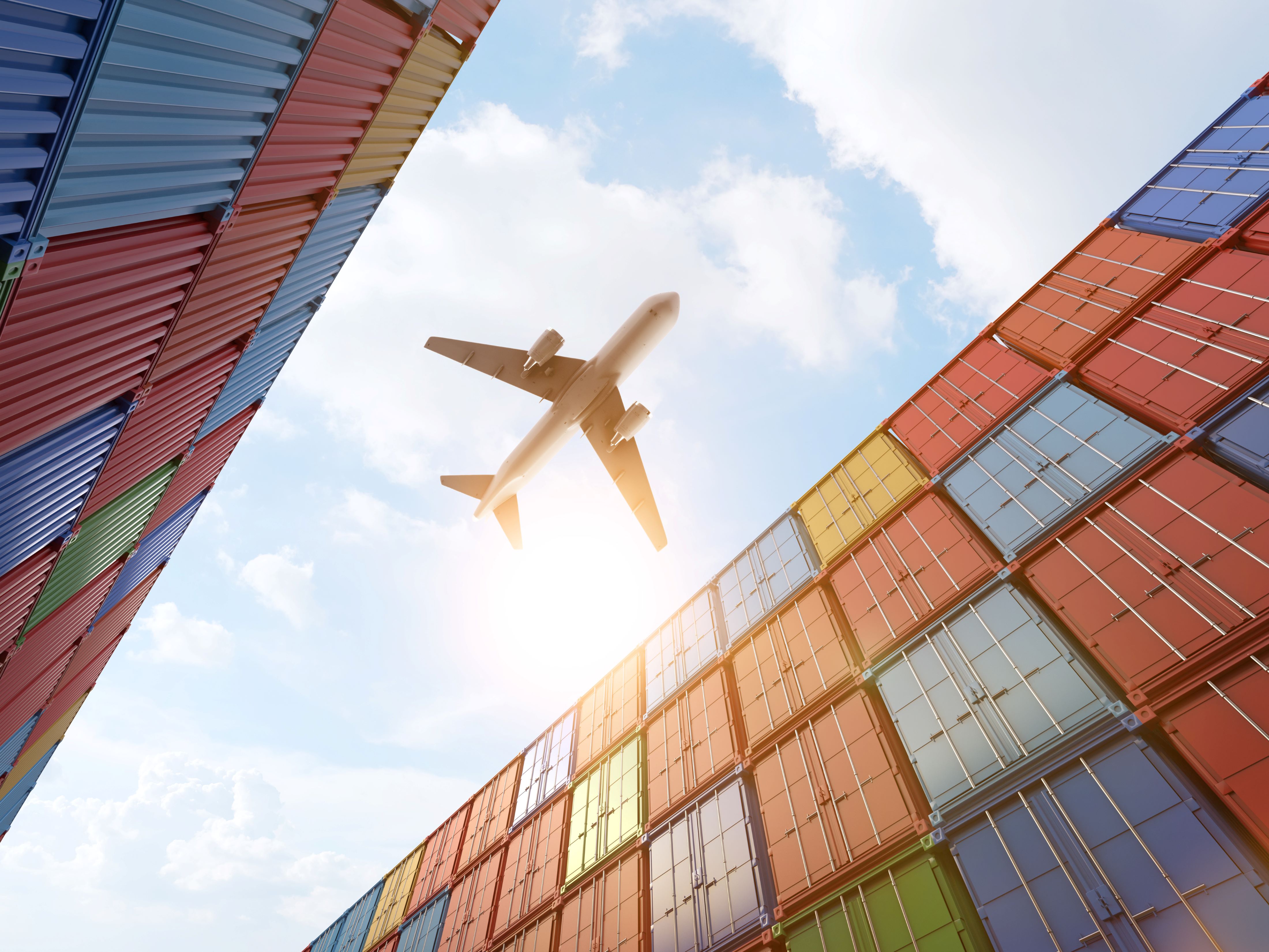 An aircraft overhead between stacks of shipping containers