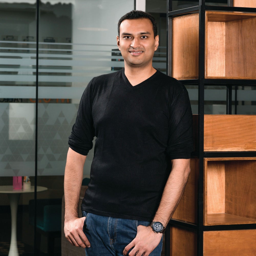 Dhruvil Sanghvi standing beside wooden shelving in an office