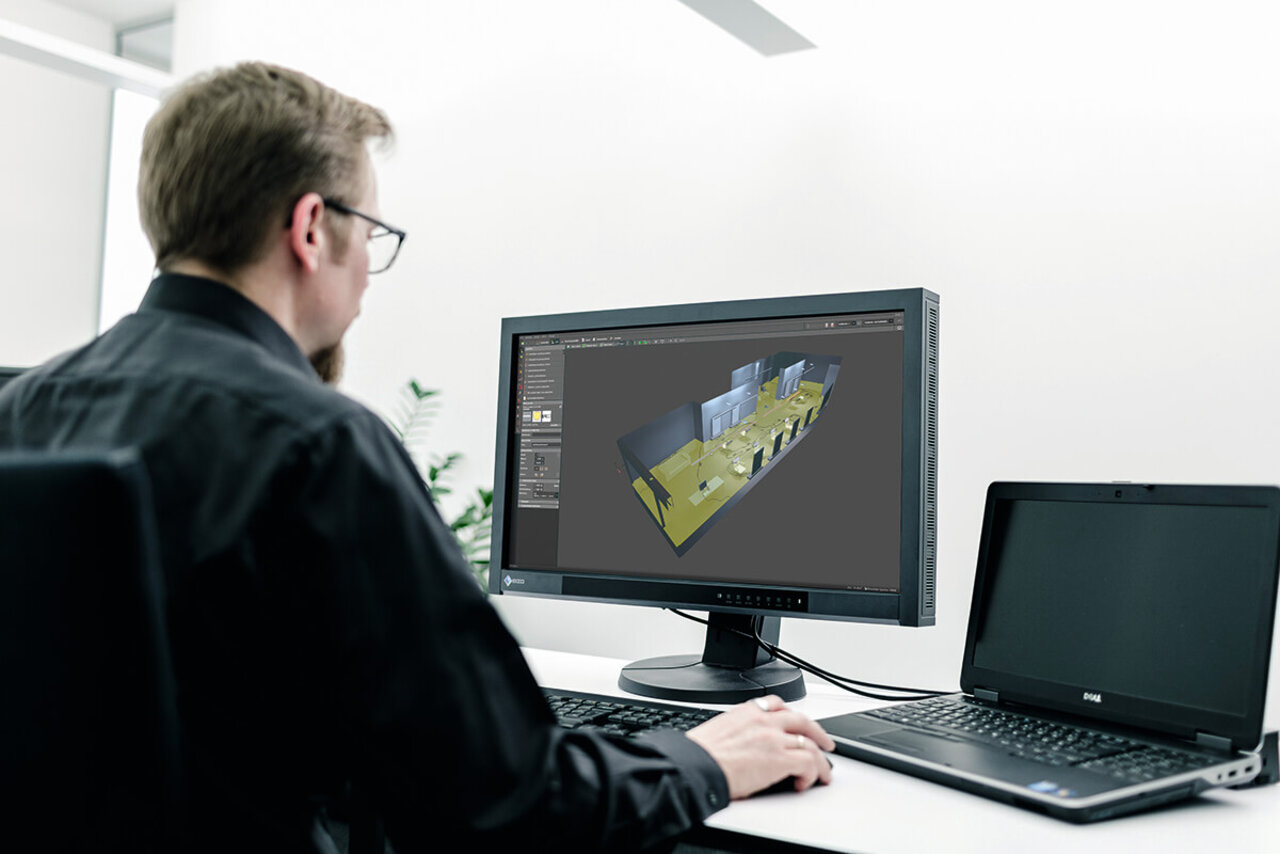 A lighting planner examines a building model in DIALux on a desktop monitor