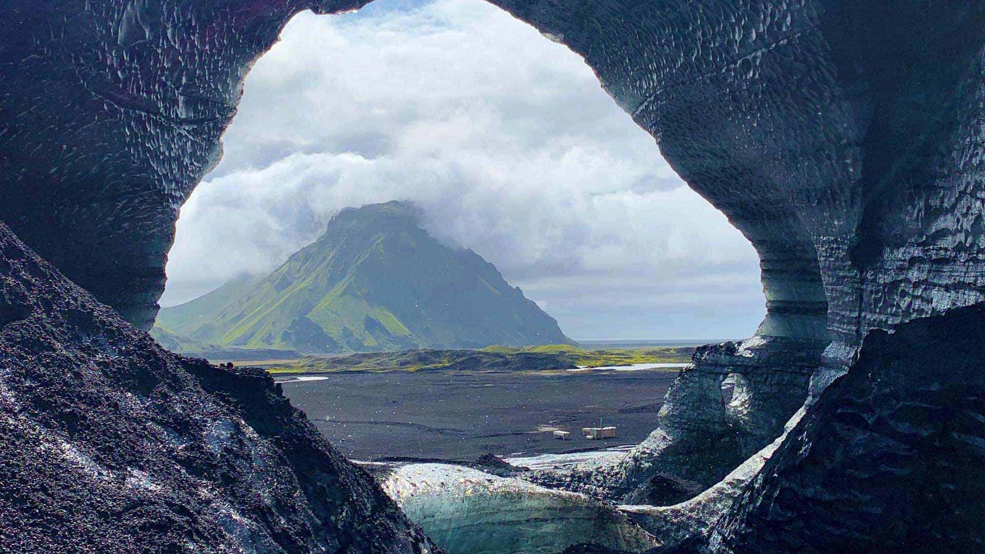 A green mountain framed by a dark volcanic cave in Iceland