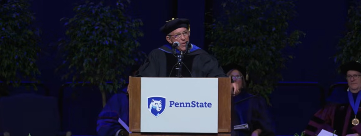 Dick Lippin speaking at a Penn State lectern during the 2026 College of the Liberal Arts commencement