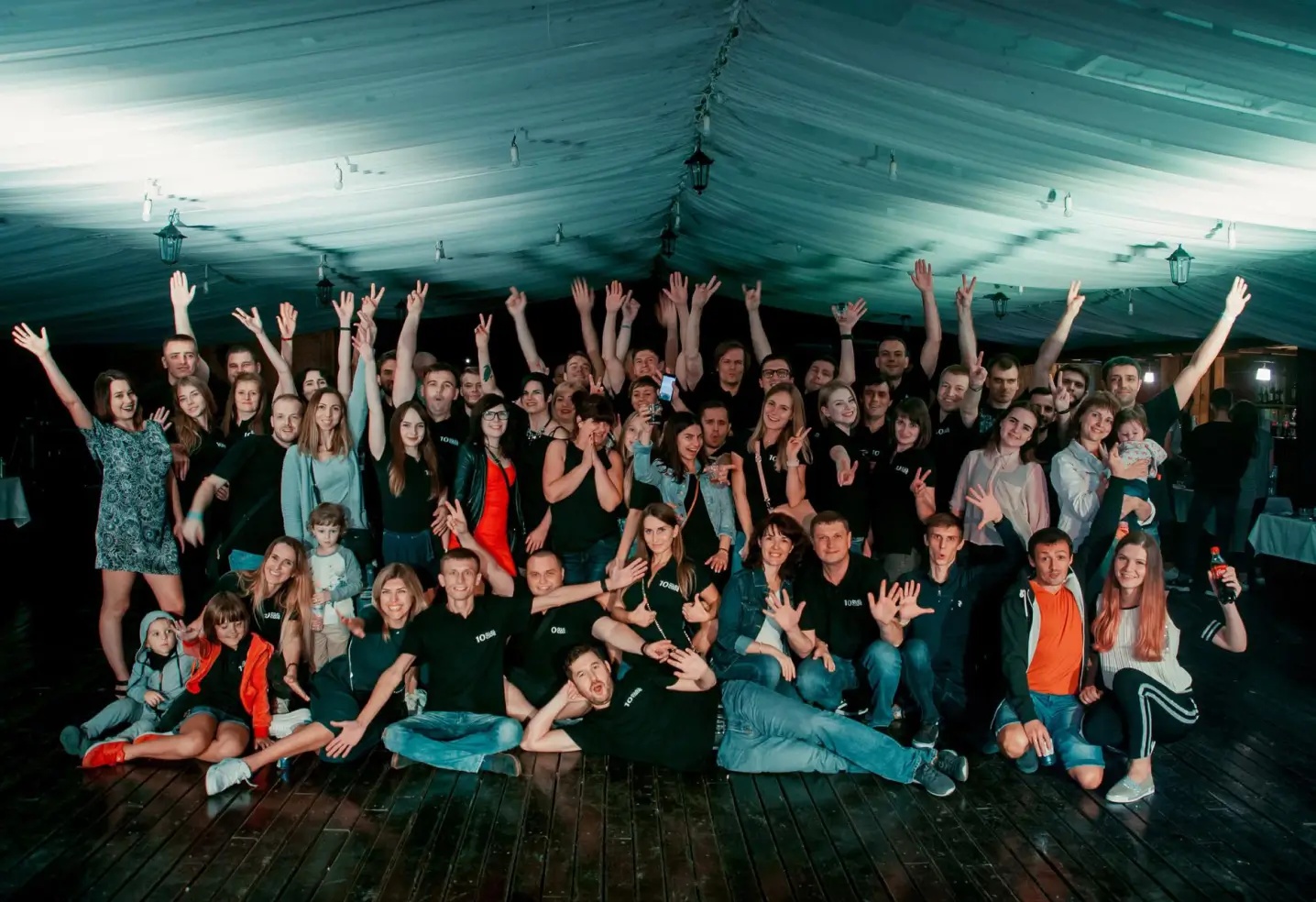 Digicode team and family members gathered beneath a tent, many waving at the camera