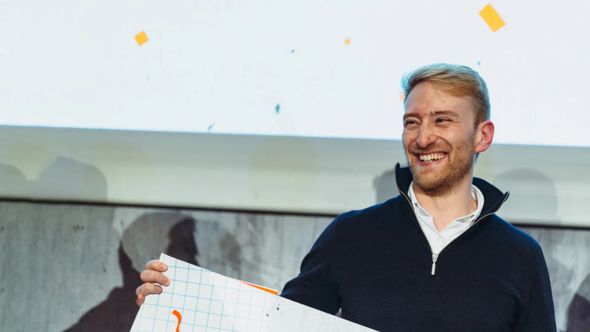 A smiling participant holding a presentation board beneath falling confetti at an Ignition pitch battle