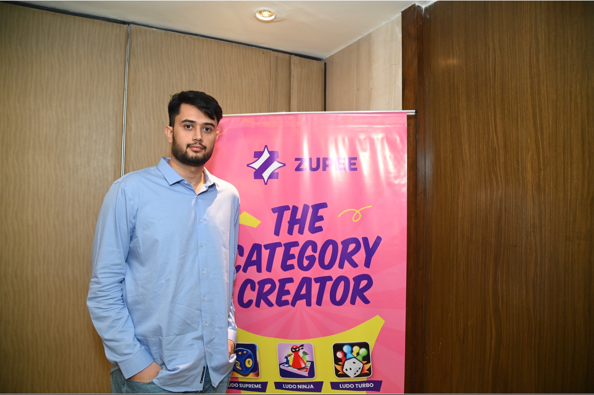 Dilsher Singh Malhi standing beside a pink Zupee banner displaying its Ludo games