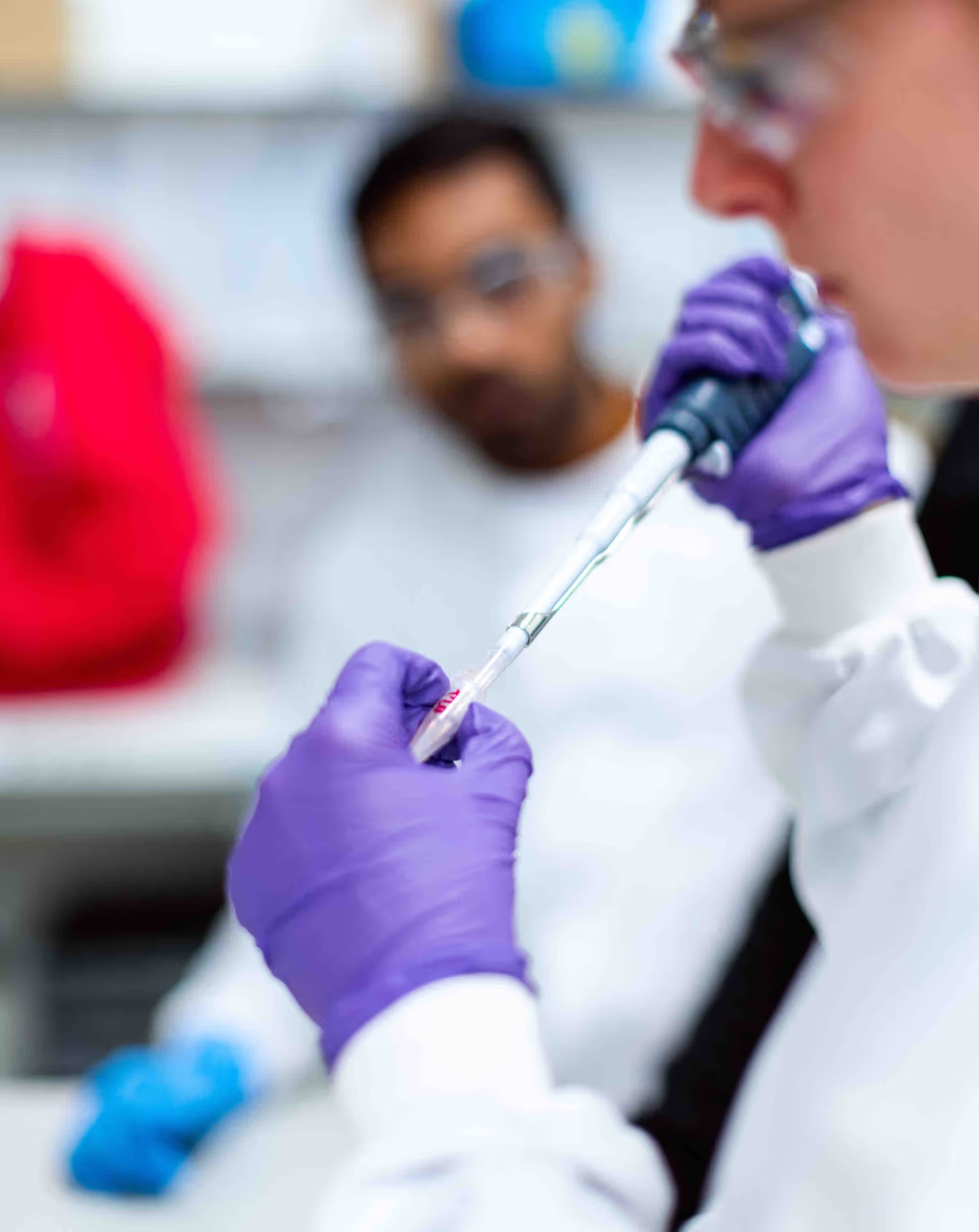 Researcher in safety glasses and purple gloves transferring liquid with a pipette