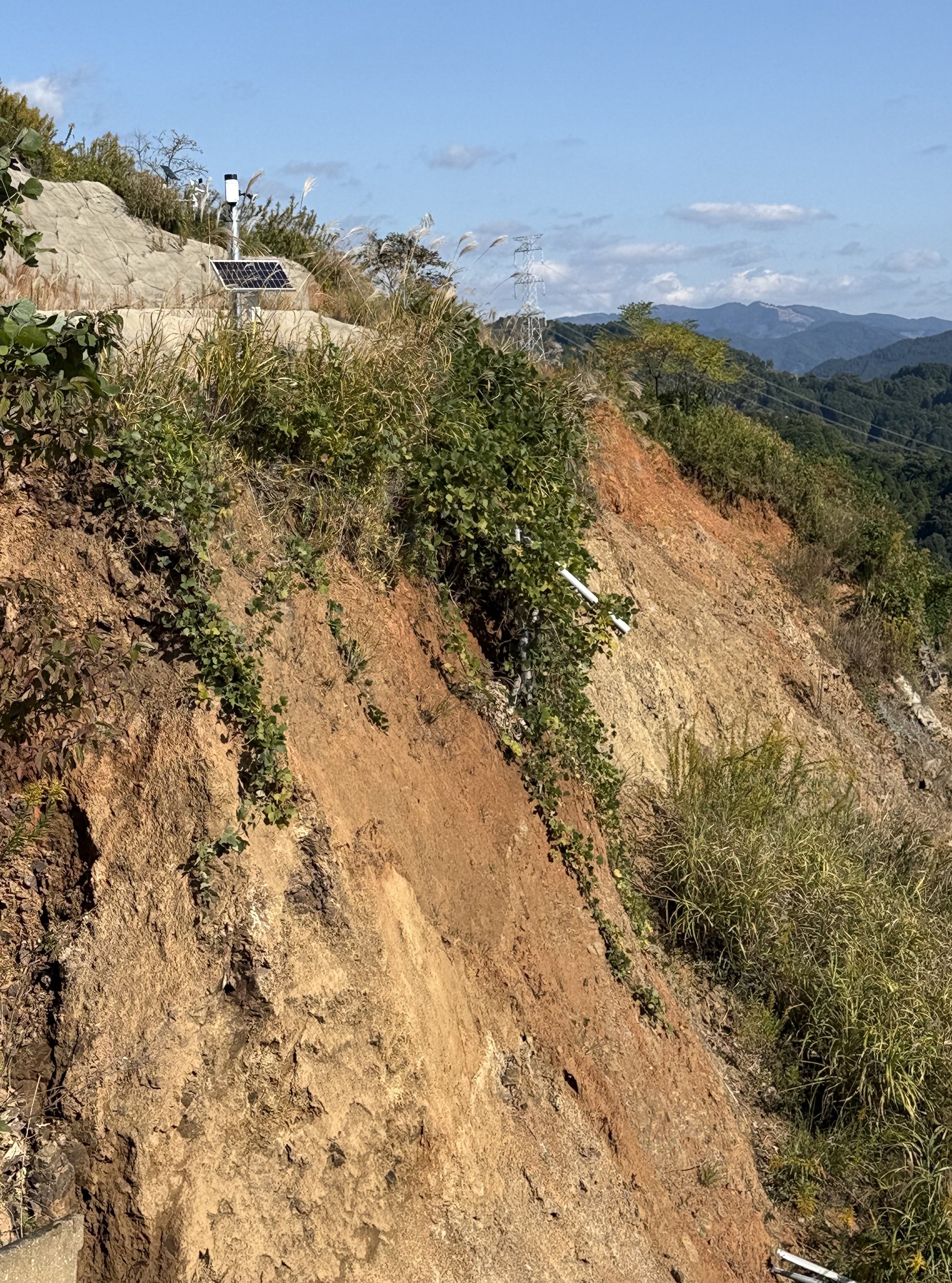 A solar-powered Divirod monitoring sensor installed above a steep exposed slope in Fukuoka Prefecture, Japan