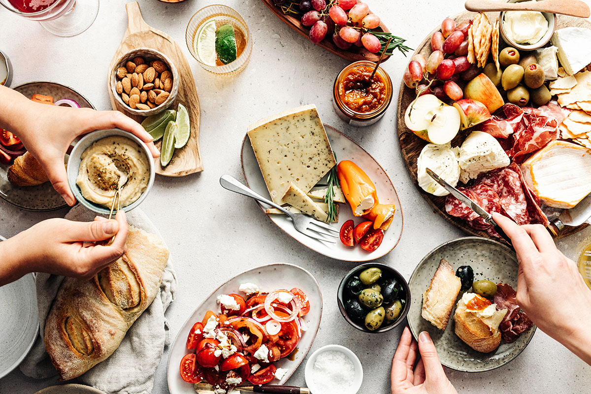 An overhead table spread with fruit, vegetables, bread, cheese and dips