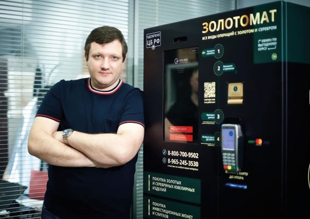 Dmitry Plushevsky standing beside a GOLDEX gold exchange terminal
