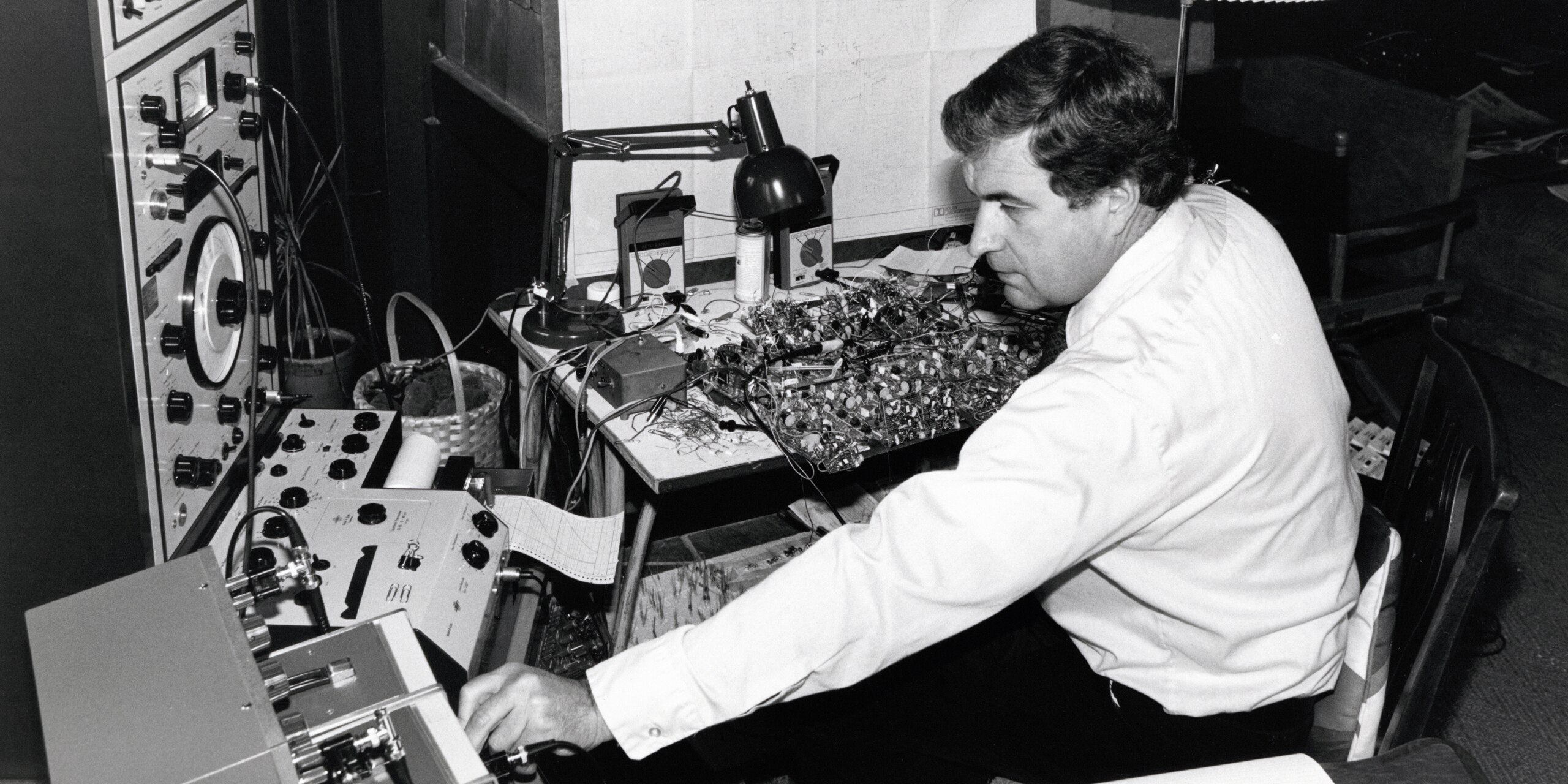 Ray Dolby working at a crowded electronics bench surrounded by test equipment