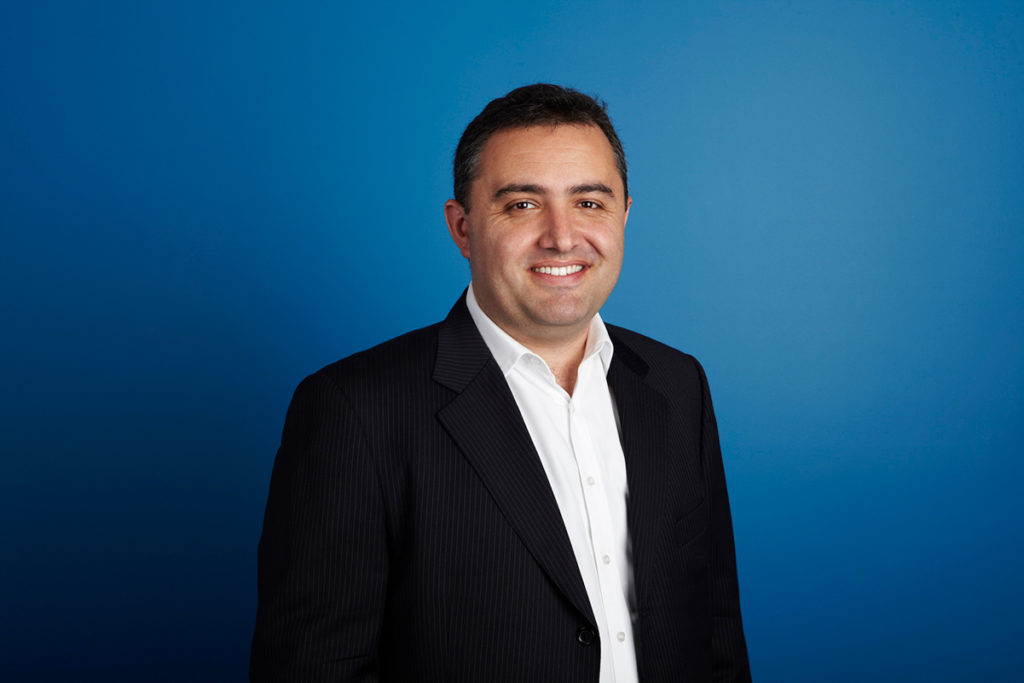 Jason Pellegrino wearing a dark suit against a blue background