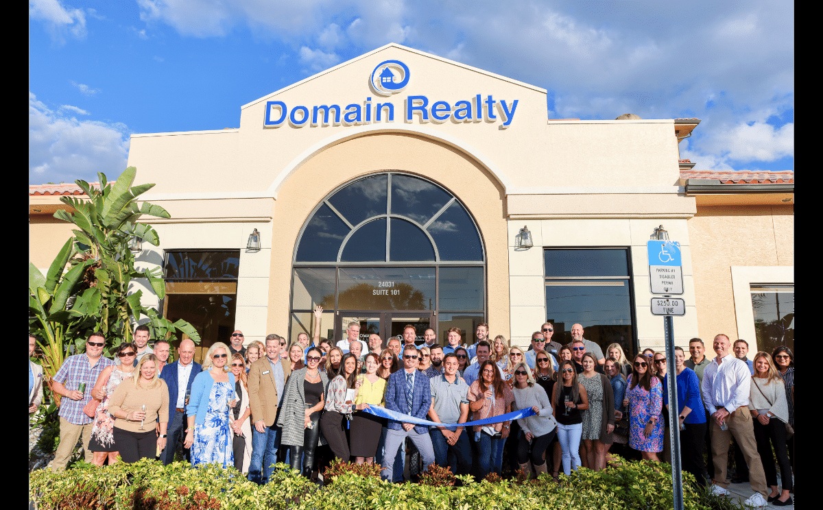 A group gathered with a blue ribbon outside Domain Realty’s Bonita Springs office