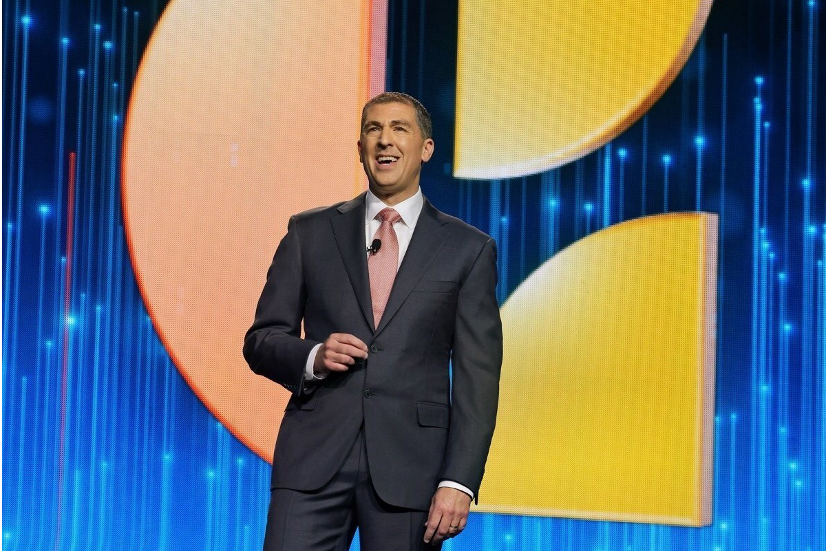 Dominic Dragisich speaking onstage in front of a blue and yellow backdrop at Choice Hotels’ 70th Annual Convention