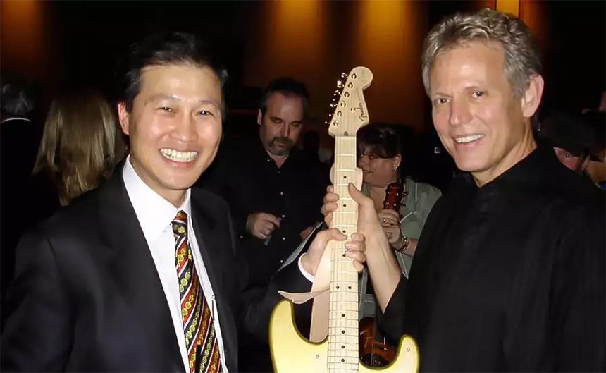 Dominic Ng and Don Felder smiling beside a guitar at a 2006 Katrina benefit concert