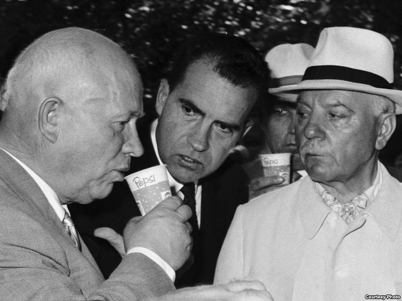 Nikita Khrushchev drinking from a Pepsi cup as Richard Nixon watches at the 1959 Moscow exhibition