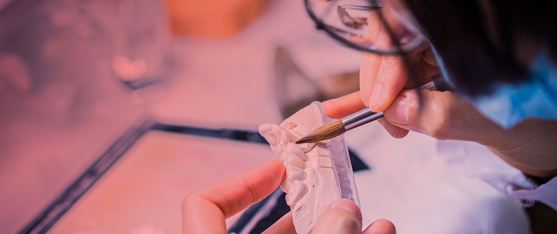 Close-up of a laboratory craftsperson using a fine brush on a dental model