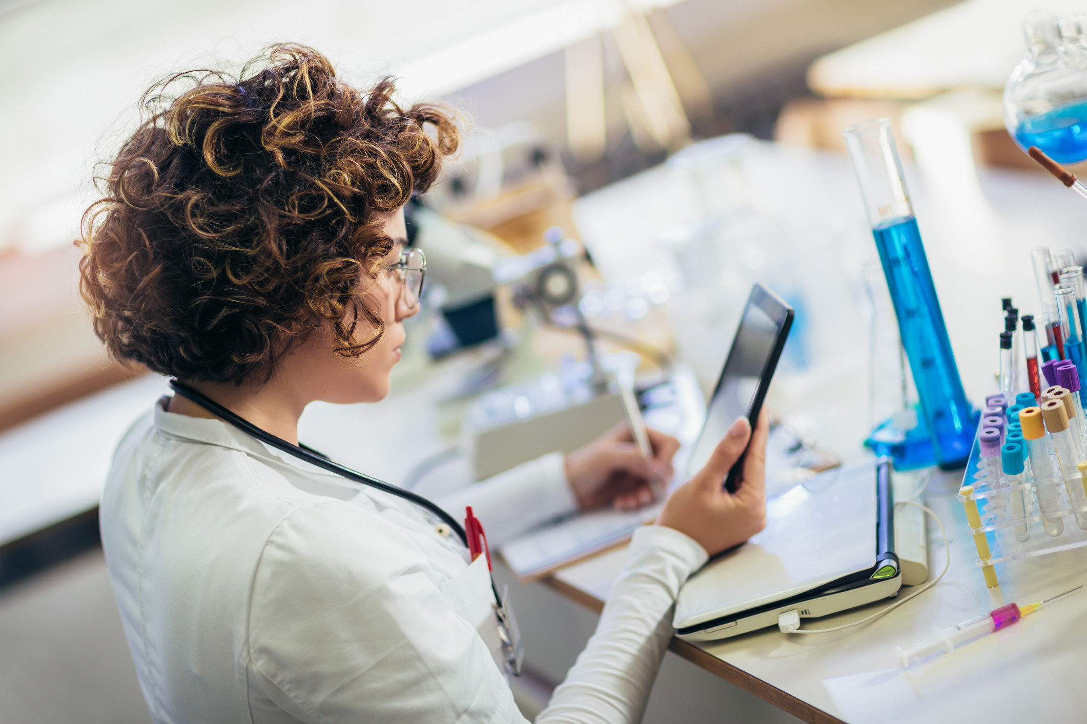 A scientist consults a tablet beside laboratory glassware and sample tubes