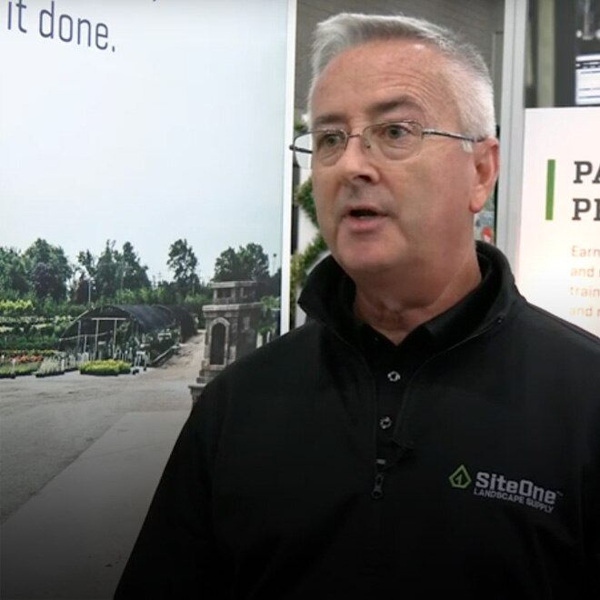 A SiteOne representative in a black company jacket speaking at a trade-show booth