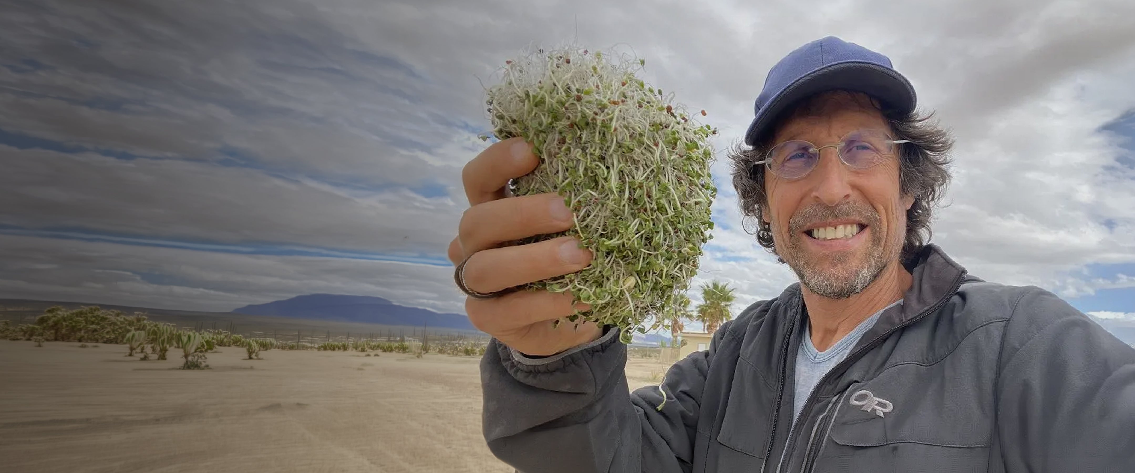 Doug Evans holding fresh sprouts outdoors against a desert landscape