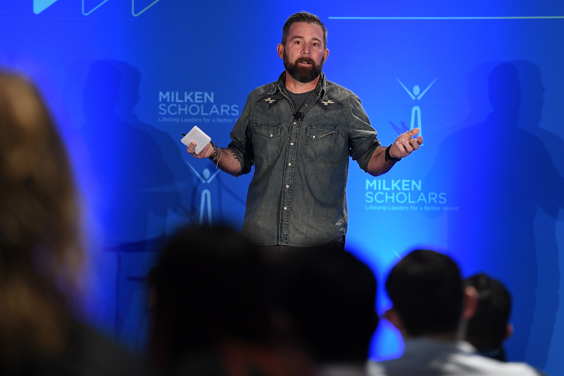 Doug Hirsch speaking onstage at the 2023 Milken Scholars Alumni Symposium, holding notes and gesturing to the audience